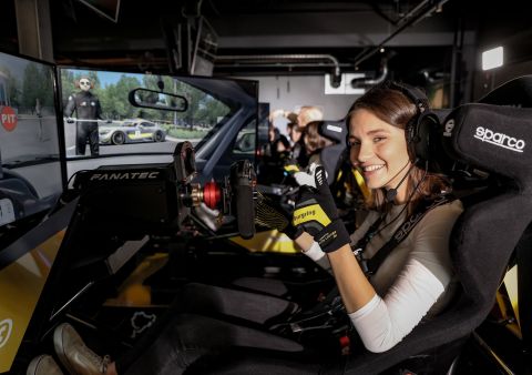 Eine Frau sitzt in einem Rennsimulator und zeigt lächeln mit dem Daumen nach oben