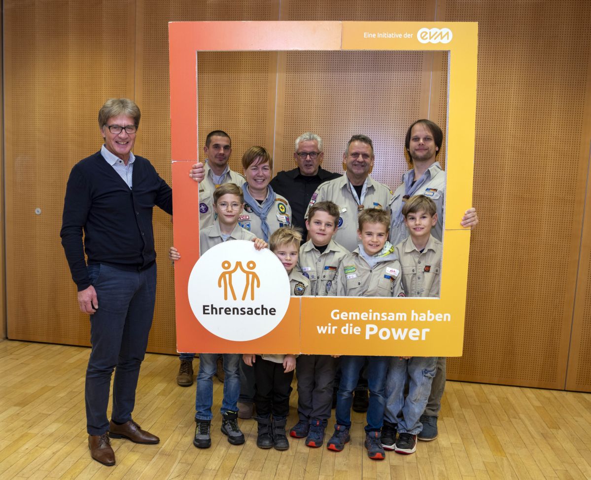 Kaisersesch_82 Eine Gruppe von Menschen, darunter Kinder in Pfadfinderuniformen, hält einen großen Bilderrahmen. Auf dem Rahmen steht: "Ehrensache - Gemeinsam haben wir die Power". Sie stehen in einem Raum mit Holzverkleidung.