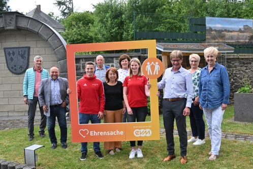 Fünf Männer und fünf Frauen lächeln freundlich und halten einen orangenen Rahmen mit der Aufschrift "Ehrensache".