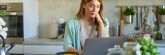 Young cheerful woman using laptop computer and eating cornflakes in the kitchen at home