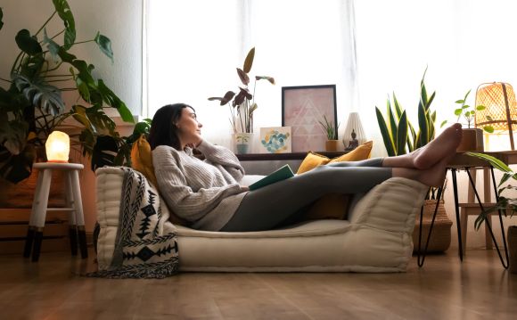 Pensive woman relaxes at home lying on sofa looking out the window. Copy space. Lifestyle concept.