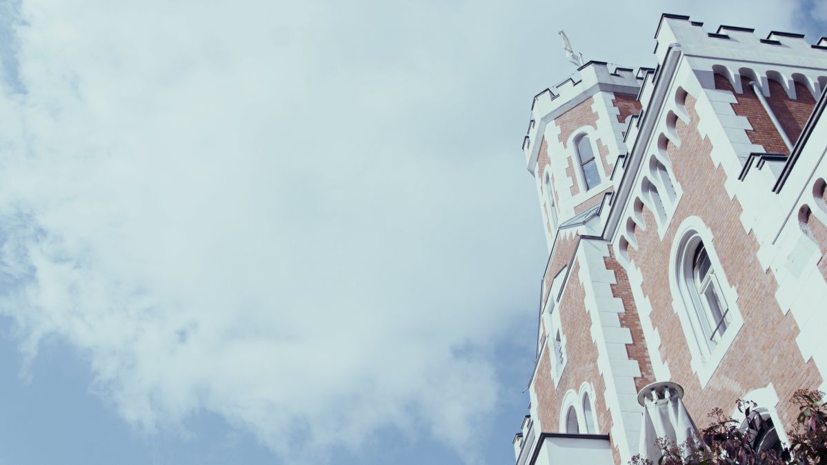 Ein historischer Turm aus rotem Backstein mit weißen Verzierungen ragt in den Himmel. Der Turm ist von leicht bewölktem Himmel umgeben, bei klarem Wetter.