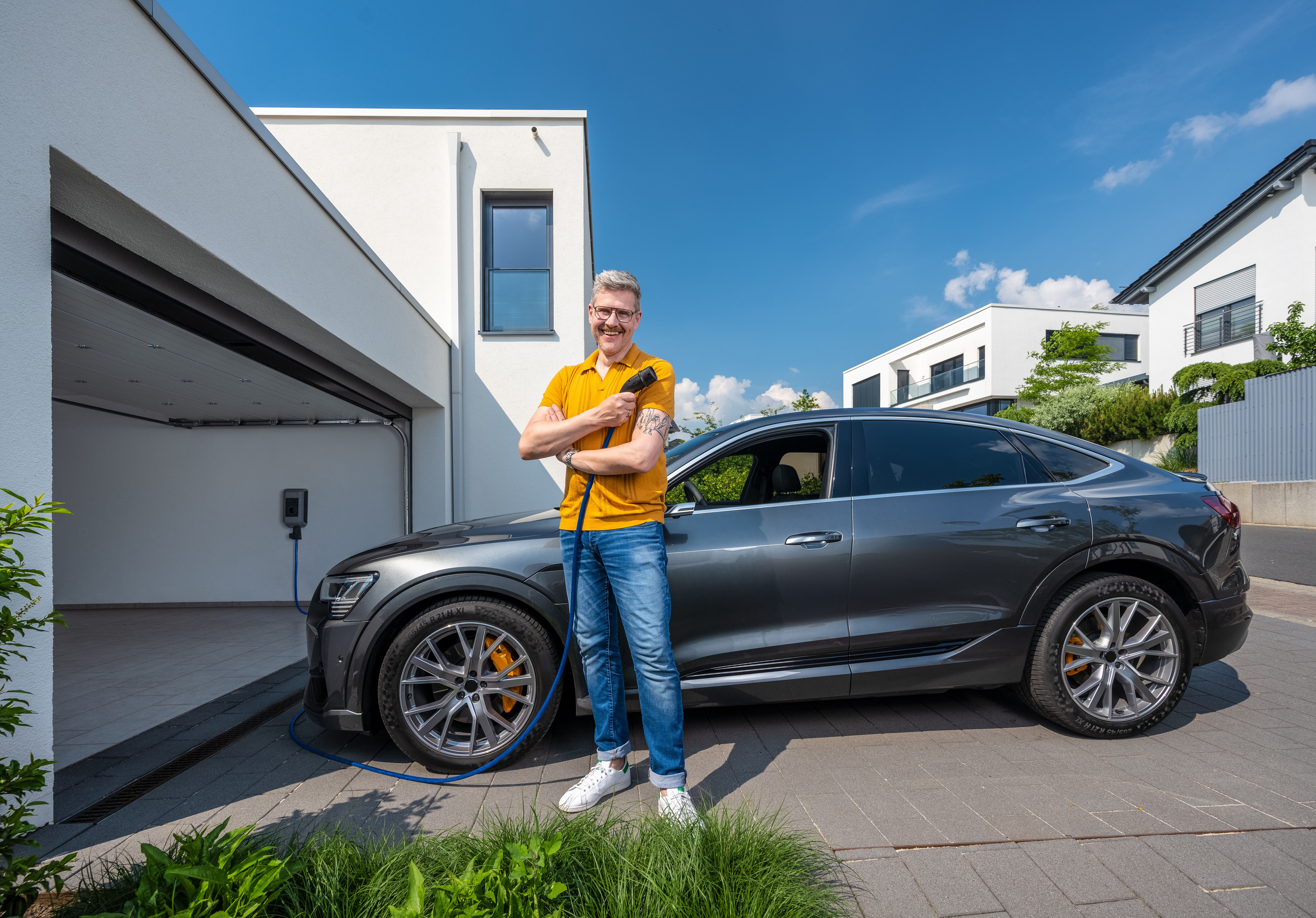 Mann vor Elektroauto hält Ladekabel der Wallbox in der Hand