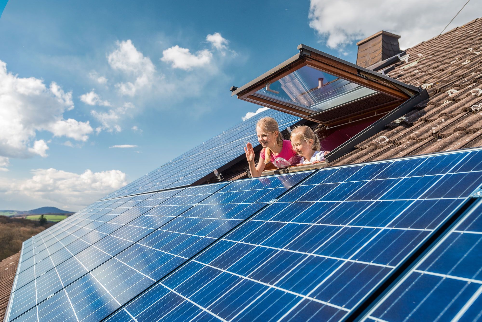 Kinder schauen aus einem Dachfenster auf die Solaranlage.