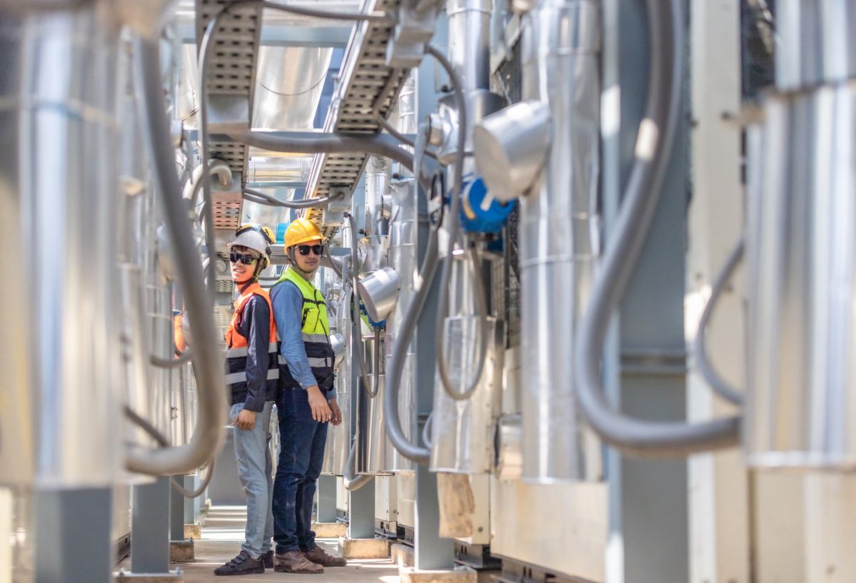 Industriestrompreis als Chance: Kurzfristige Entlastung für energieintensive Unternehmen Zwei Fachkräfte in Schutzkleidung stehen in einer industriellen Umgebung, umgeben von großen Rohrleitungen und technischen Anlagen.