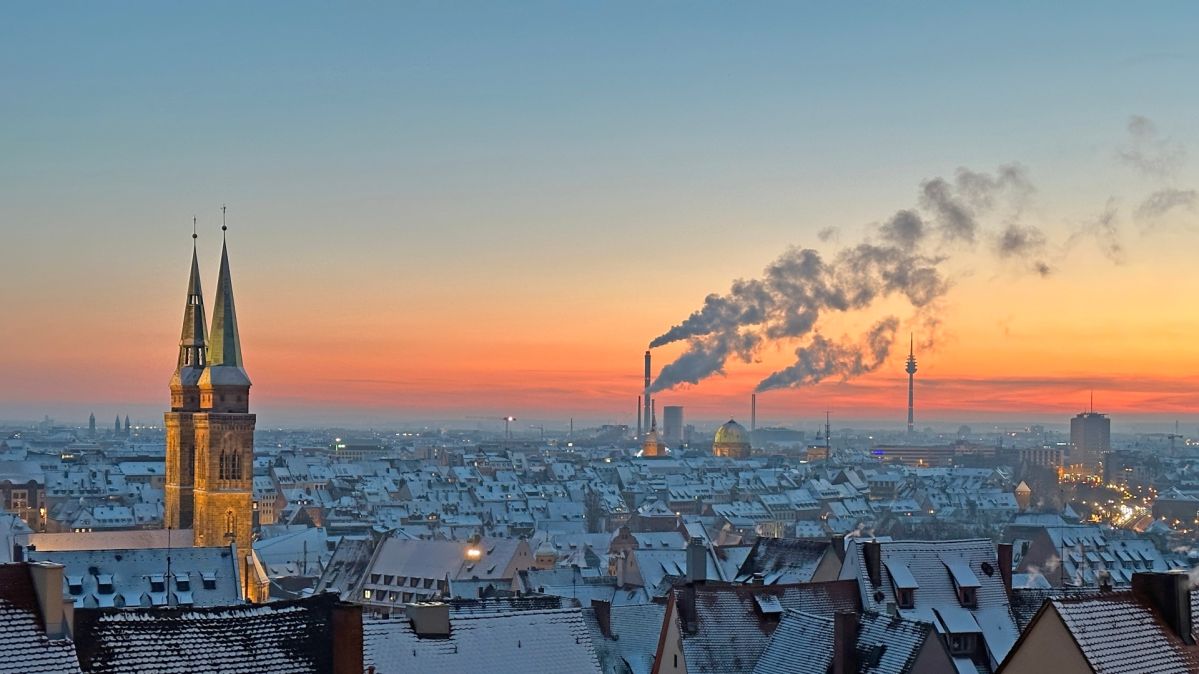 Leichter Anstieg beim Energieverbrauch – Deutschland bleibt auf Klimakurs Die Silhouette einer Stadt im Winter, Rauch steigt in der Ferne auf