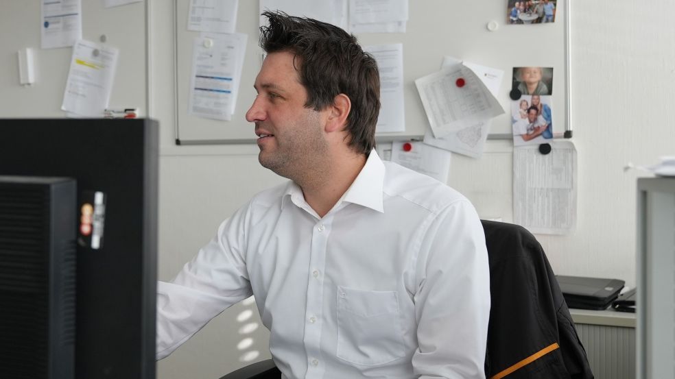 Energieberatungen können auch während aktuell durchgeführt werden. Ein Mann sitzt an einem Schreibtisch und arbeitet am Computer. Der Raum ist mit einem Whiteboard voller Notizen im Hintergrund ausgestattet. Ordner und Papiere liegen herum.