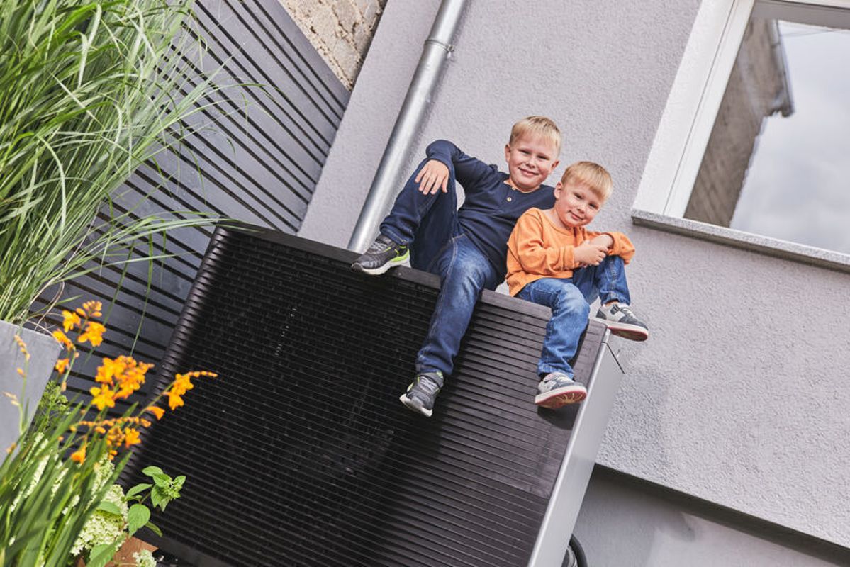 Zwei Jungs sitzen auf dem Außenelement einer Wärmepumpe