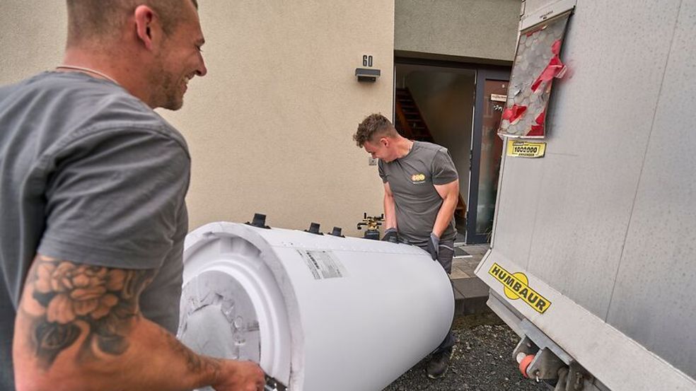 Zwei Monteure der evm Service GmbH tragen die neue Wärmepumpe ins Haus.