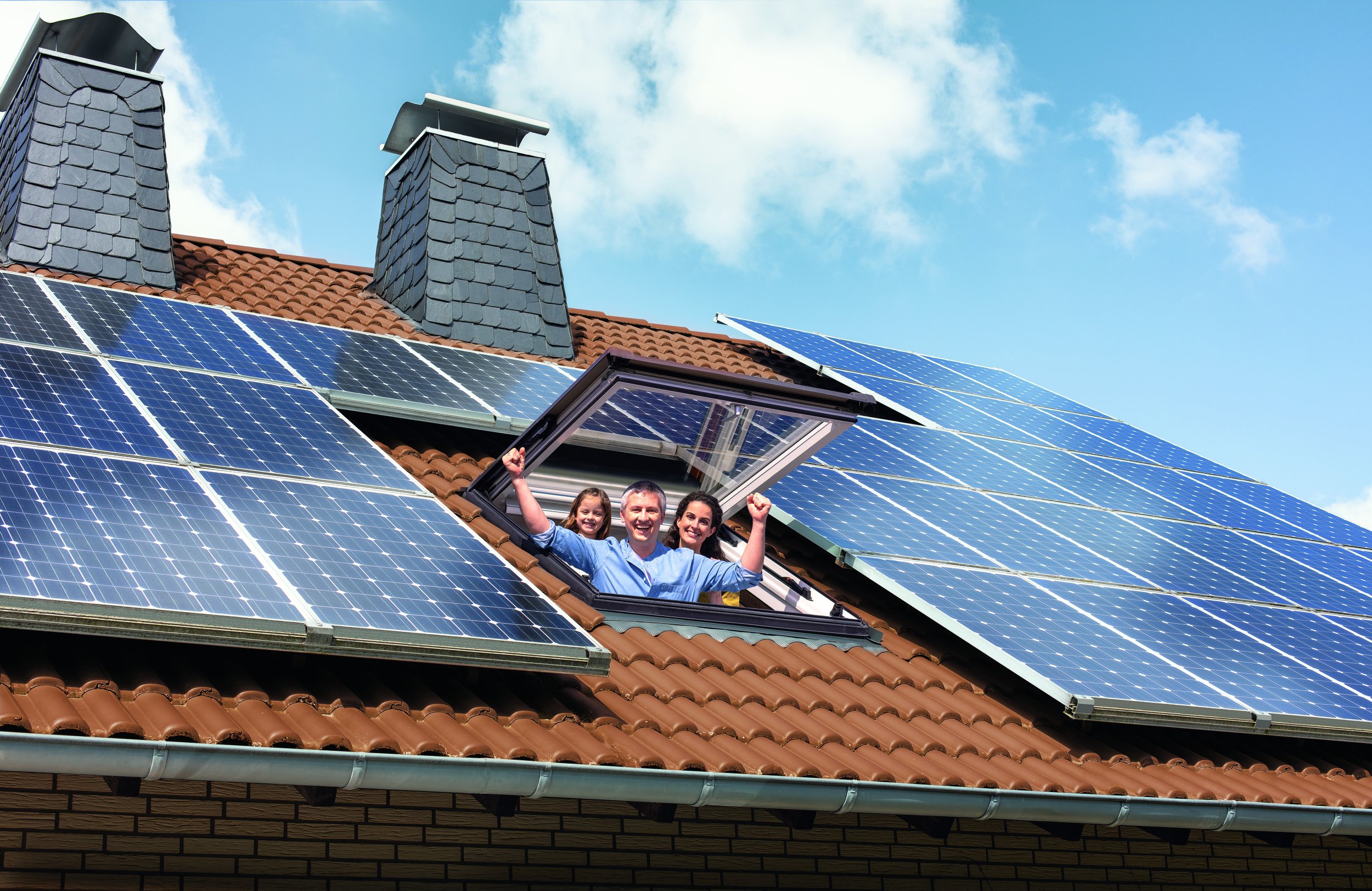Ein Mann, eine Frau und ein Kind schauen aus einem Dachfenster. Auf dem Dach befinden sich mehrere Solarmodule.