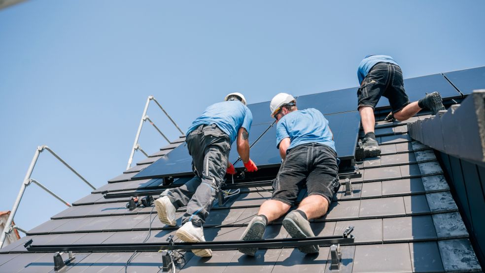 Zwei Monteure installieren eine PV-Anlage auf einem Schieferdach