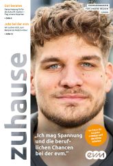 Ein Mann mit Bart lächelt leicht. Links steht vertikal „Zuhause“. Der Hintergrund ist unscharf.