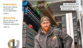 Ein Mann in Arbeitskleidung mit rotem Bart steht vor gestapelten Kisten in einem Lager.