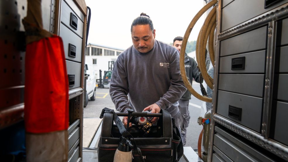 Loc Tran steht zwischen geöffneten Fahrzeugtüren eines Servicefahrzeugs und kontrolliert, ob seine Ausrüstung vollständig ist.