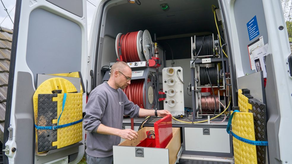 Arbeiten unter Strom Das geöffnete Heck eines Kabelmesswagens zeigt eine gut organisierte Innenausstattung mit mehreren großen Kabeltrommeln in Rot und Schwarz. Bernhard Hofer steht am Fahrzeug und hantiert mit einem roten Werkzeugkoffer. Im Inneren sind verschiedene Fächer und technische Geräte zur Kabeldiagnose sichtbar.