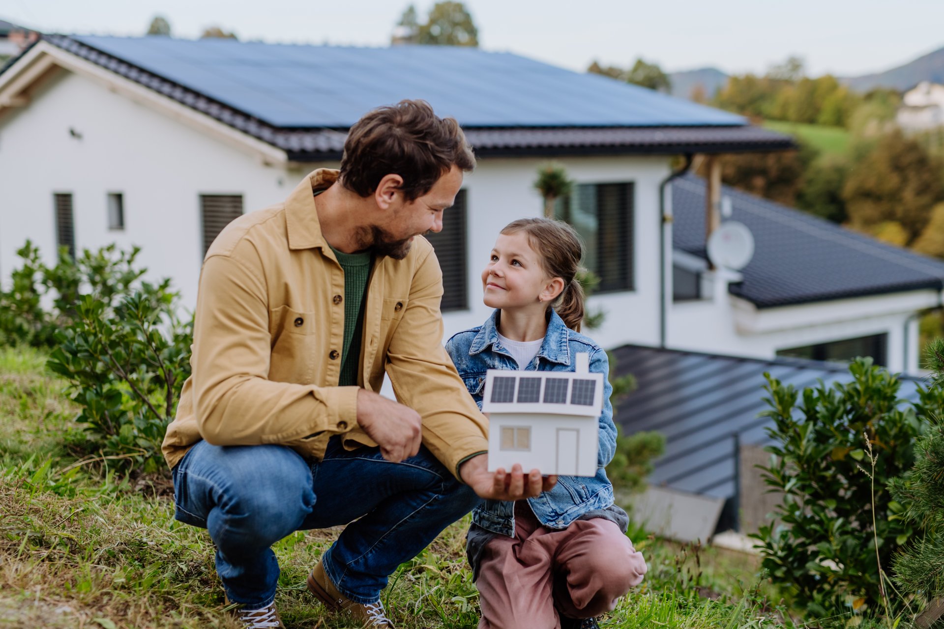 Ein Jahr Strom geschenkt – so einfach geht’s mit deiner Solaranlage von der evm Ein Vater steht mit seiner kleinen Tocher vor ihrem Einfamilienhaus, das Solarmodule auf dem Dach hat
