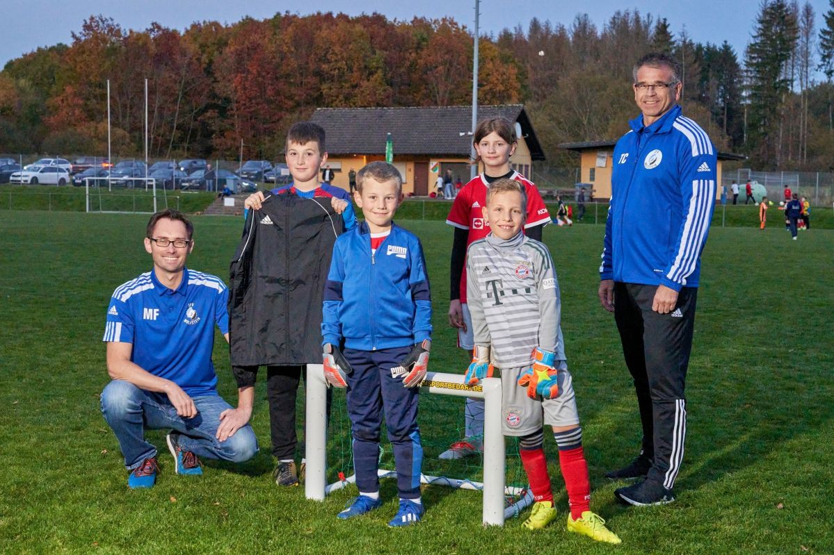 Einige Kinder und die Geschäftsführer stehen vor einem kleinen Fußballtor.