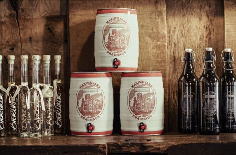 Hier braut sich was zusammen: Das Maximilians Brauwiesen überzeugt durch traditionelle Braukunst Drei Fässer Bier umringt von einigen Gläsern und Flaschen