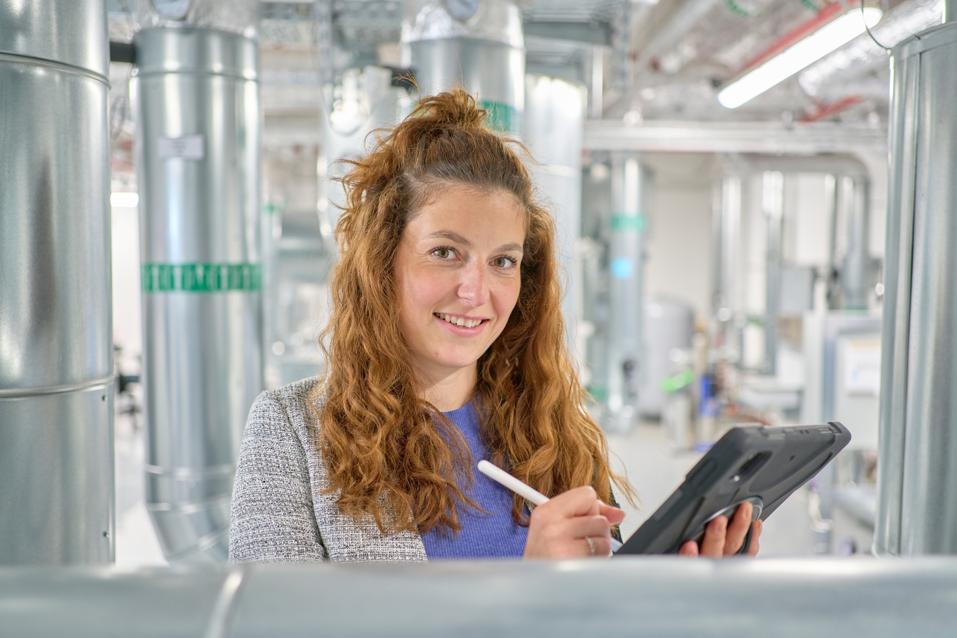 Energieeffizienz im Einsatz Valerie Schmitz bei der Arbeit: Mit dem Tablet dokumentiert sie vor Ort energetische Verbrauchsdaten. Im Hintergrund sind große Rohrleitungen und industrielle Anlagen zu sehen.