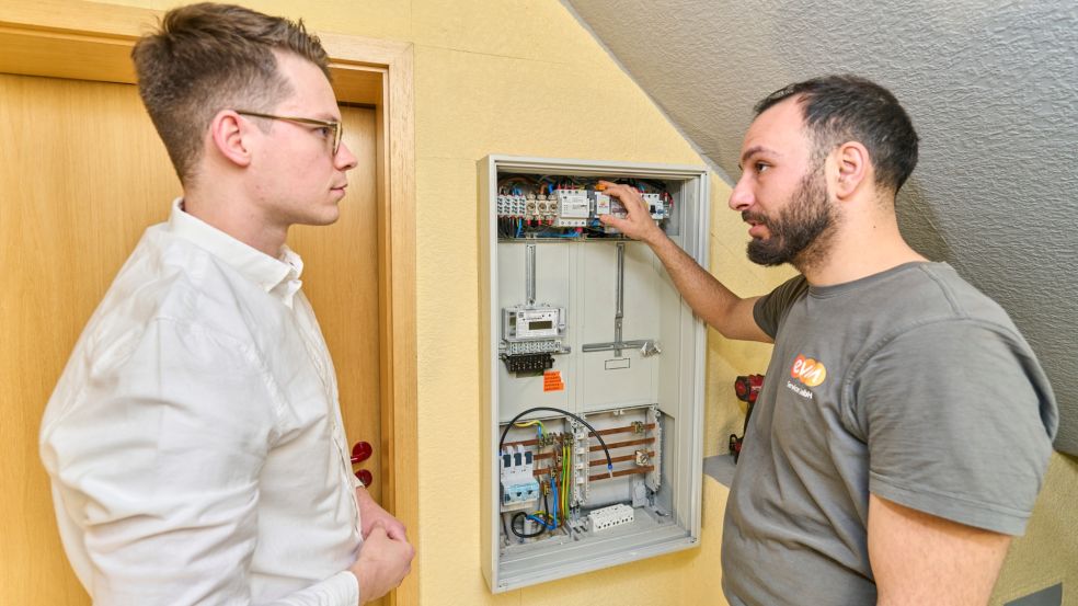 Ein Tag mit Nicolai Kretz Zwei Personen stehen vor einem offenen Elektroschaltkasten. Eine Person zeigt auf die Technik im Inneren.
