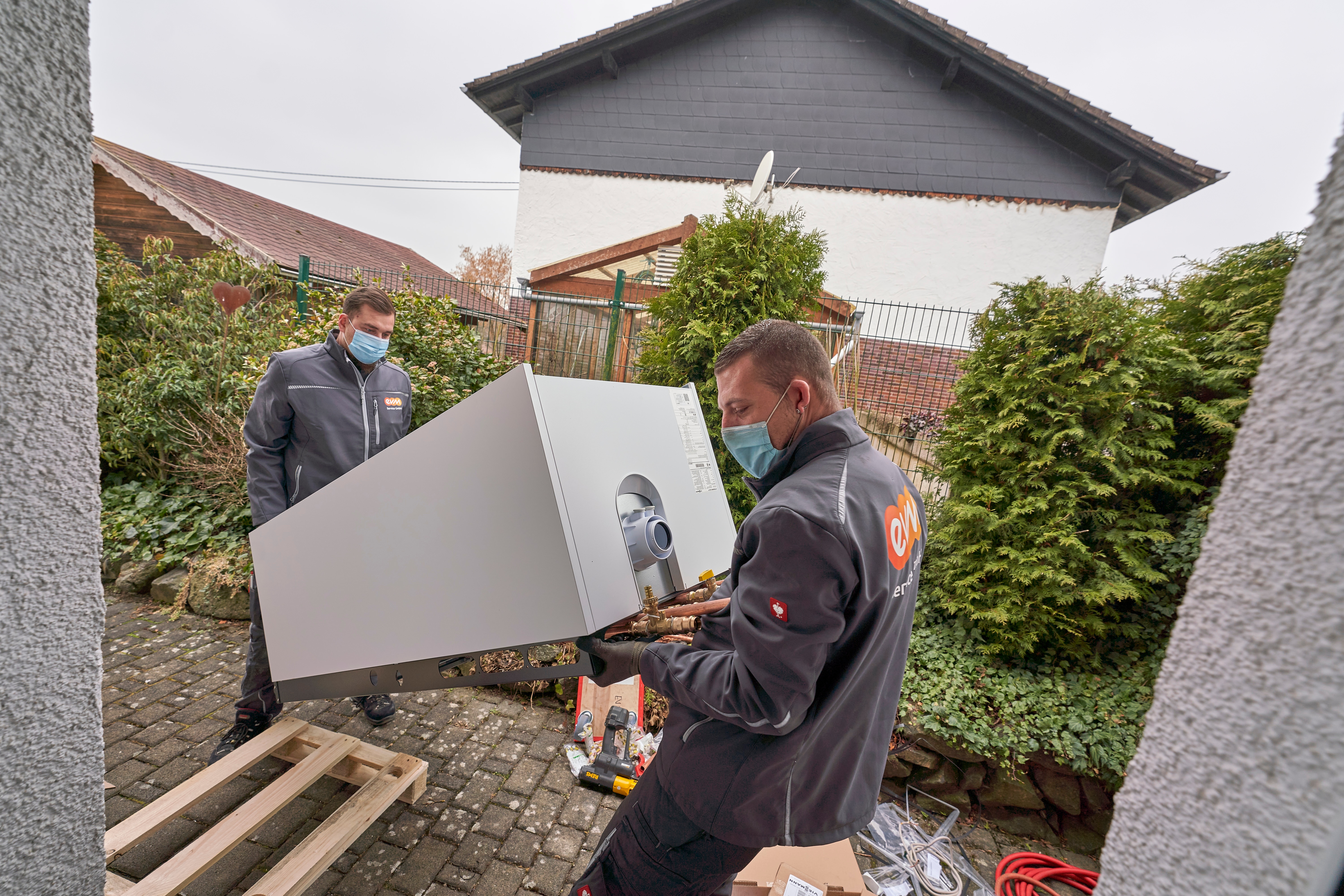 Trotz einiger Herausforderungen kann die neue Heizung problemlos eingebaut werden Zwei Monteure tragen die neue Heizanlage in das Haus des Kunden