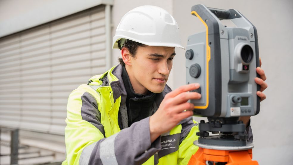Mit dem Tachymeter werden Gelände vermessen, die Daten kommen anschließend in ein GIS-System Geomatiker-Azubi Philip vor einem Tachymeter