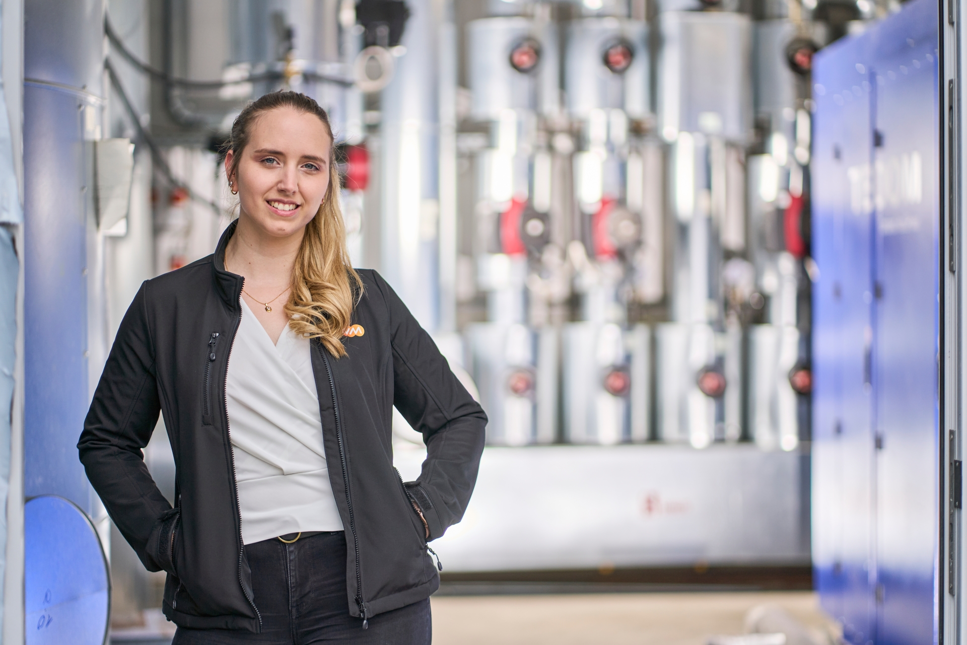 Vom Praktikum zur Projektleitung Nadine Kuhlmann vor technischen Anlagen: In einem industriellen Umfeld mit Rohrleitungen und Ventilen zeigt sich ihr Einsatz für eine nachhaltige Wärmeversorgung.
