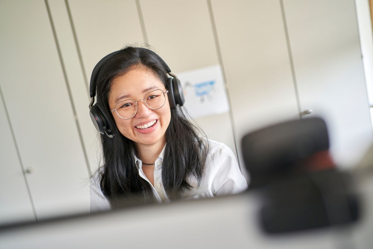 Kollegin sitzt am Schreibtisch und führt ein Teams-Meeting mit Kopfhörern durch.